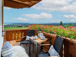 Eine Holzterrasse mit Tisch und Stühlen, die einen schönen Ausblick auf eine Landschaft mit Blumen und eine entfernte Ansicht von Häusern und Grünflächen bietet.