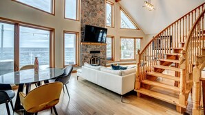 A spacious living area with a stone fireplace, a large TV, and a wooden staircase. - Lake Simcoe Waterfront Lake House (Hawkestone)