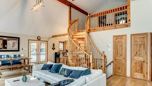 A spacious living area with a white sofa, blue cushions, a coffee table, and a wooden staircase. - Lake Simcoe Waterfront Lake House (Hawkestone)
