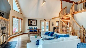 A spacious living room with a white sofa, a stone fireplace, and a wooden staircase. - Lake Simcoe Waterfront Lake House (Hawkestone)