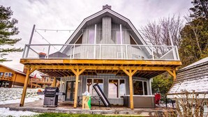 A two-story building with a balcony, wooden deck, and a covered outdoor area with a grill and hot tub. - Lake Simcoe Waterfront Lake House (Hawkestone)