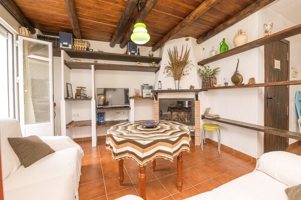Una sala de estar acogedora con techo de madera, una mesa redonda con mantel estampado y una chimenea.