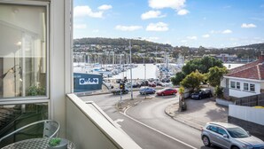 A view from a balcony overlooking a marina with boats, a road with cars, and residential buildings. - Bellerive Quay - 2 Bedroom Apartment (Bellerive)