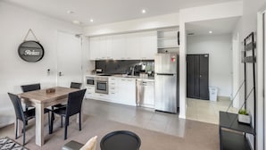 A modern kitchen with white cabinets, stainless steel appliances, and a dining area with a wooden table and chairs. - Bellerive Quay - 2 Bedroom Apartment (Bellerive)