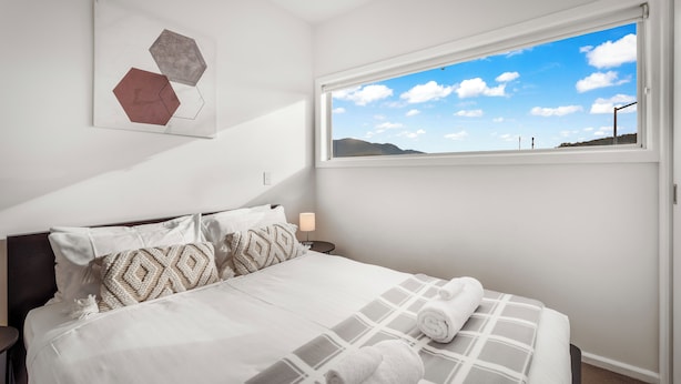 A bedroom with a large bed, a window with a mountain view, and abstract art on the wall. - Bellerive Quay - 2 Bedroom Apartment (Bellerive)
