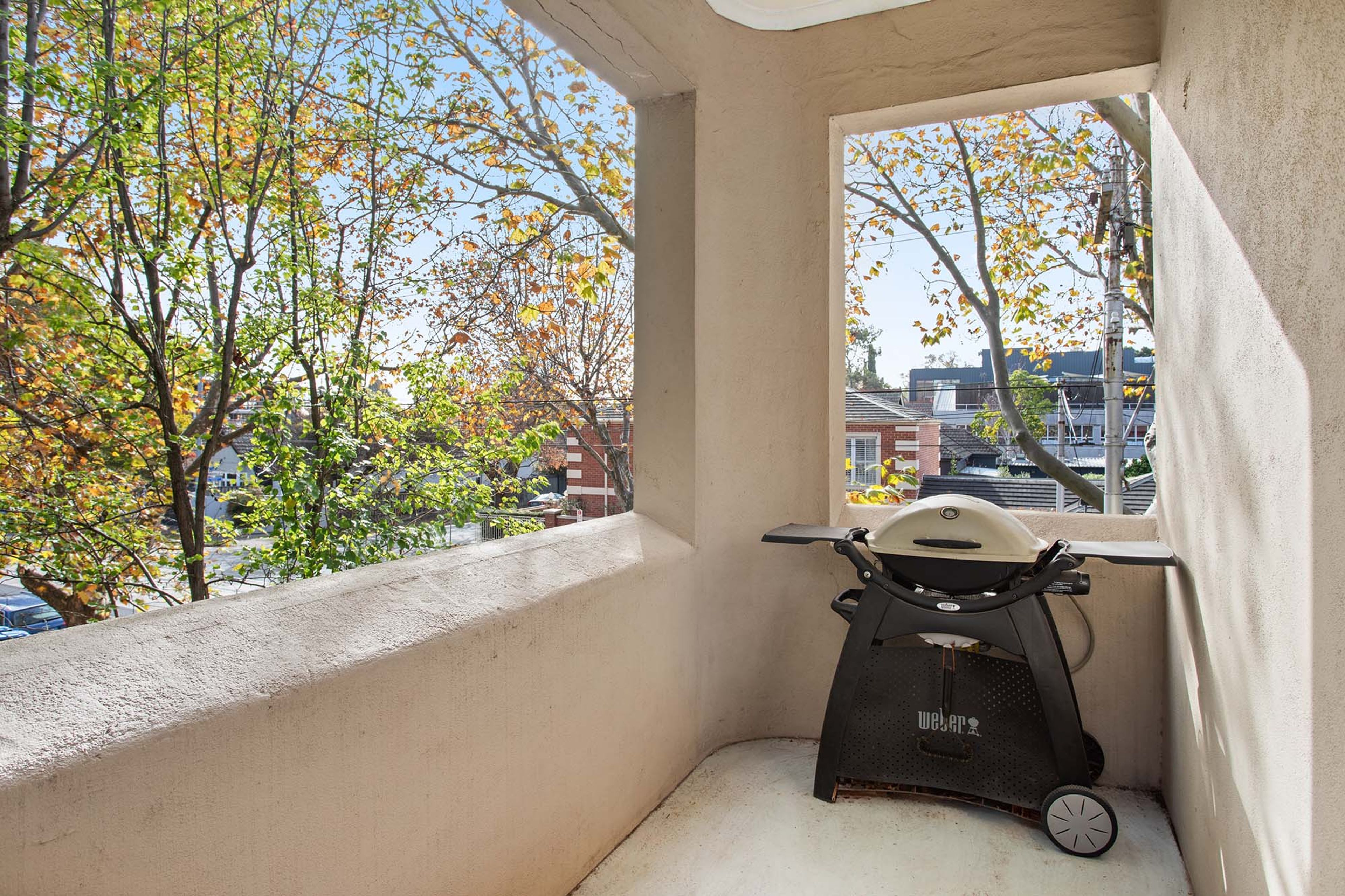 A balcony with a stationary exercise bike, a view of autumn trees, and a building in the background.