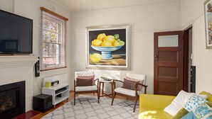 Un salon avec une cheminée, un téléviseur, un tableau représentant des citrons et un canapé jaune.