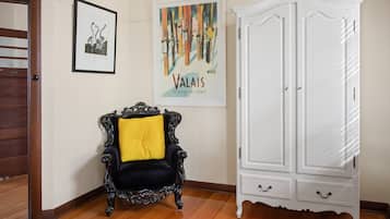 A room with a wooden floor, a black and yellow armchair, a white cabinet, and two framed artworks on the wall.