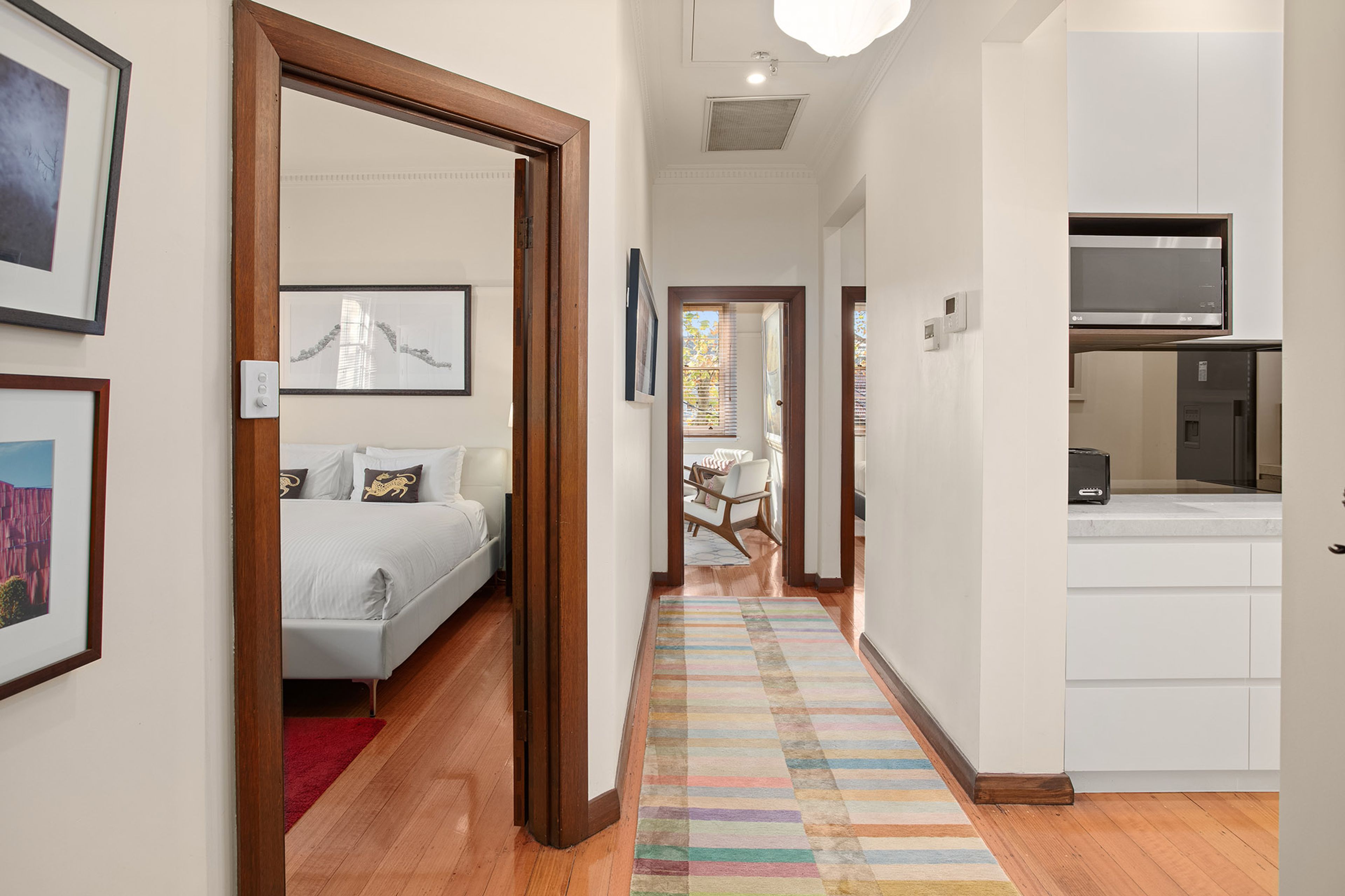 A hallway leading to a bedroom with a bed, a kitchen area with a microwave, and a dining area with a table and chairs.