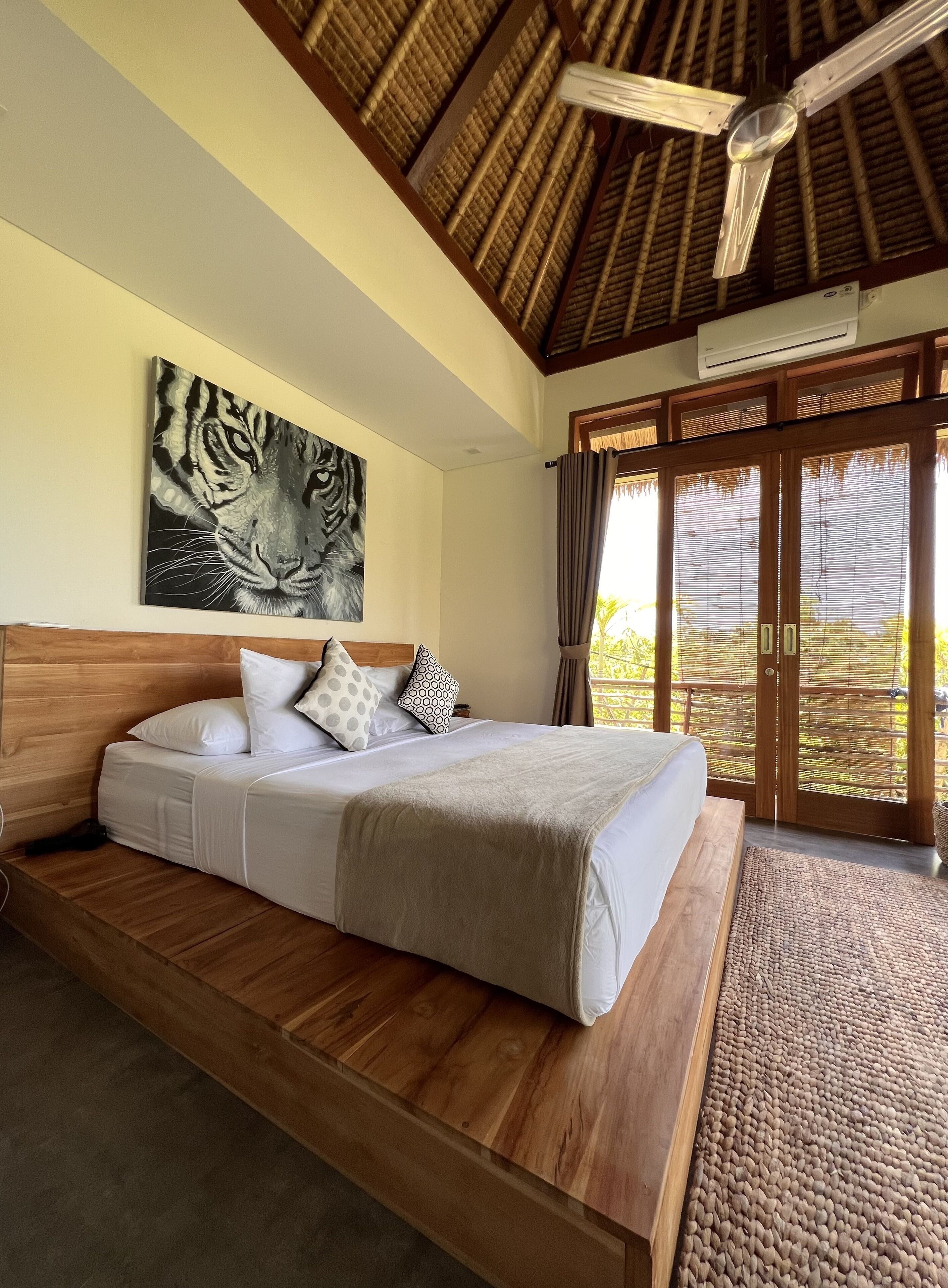 Una camera da letto con un letto di legno, un grande quadro raffigurante una tigre sulla parete e vista sul verde attraverso la porta.