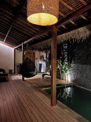 A wooden deck with a hanging light fixture, a pool, and a stone wall. - La Reserva (Jimbaran)