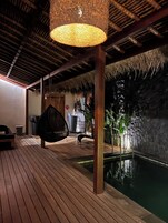 Una terraza de madera con un colgador de luces, una piscina y un muro de piedra.