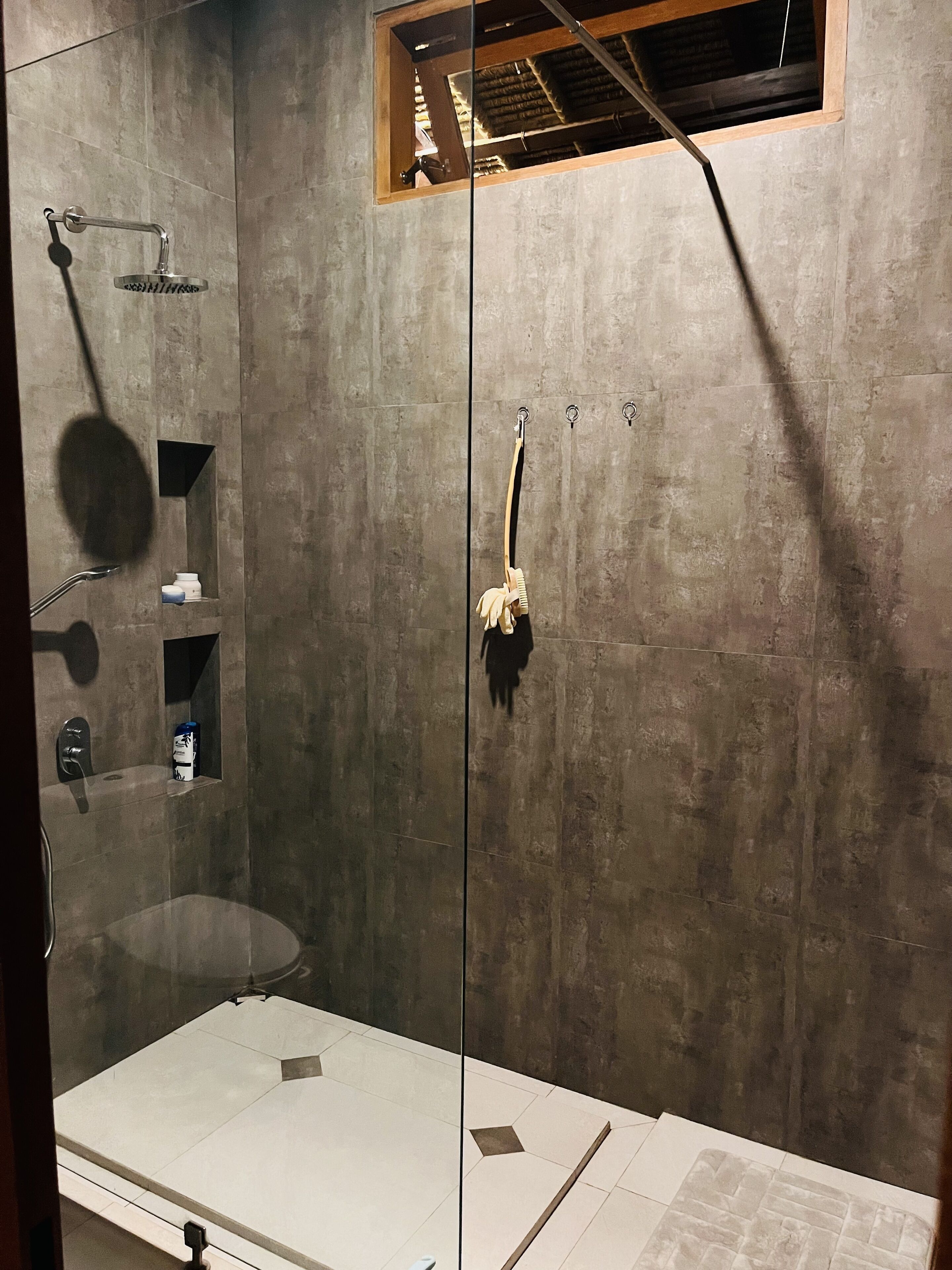 Una ducha moderna con puerta de vidrio, un perchero y un ventanal.