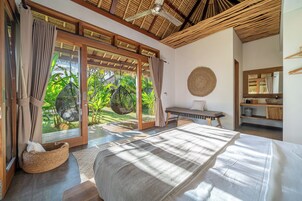 Un dormitorio con cama, un banco, una cesta tejida y vistas a la vegetación a través de grandes puertas correderas.