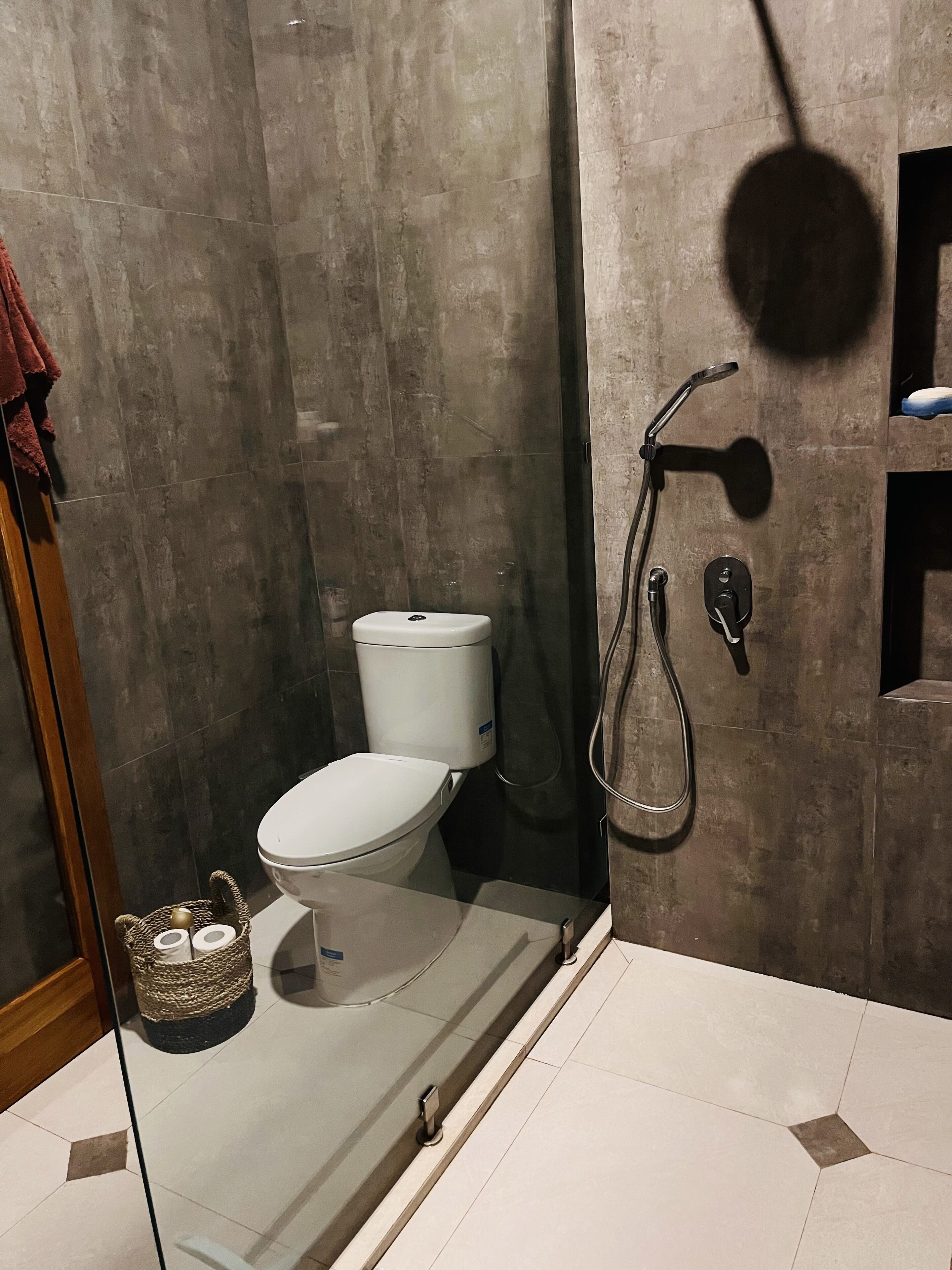 Une salle de bain moderne équipée de toilettes, d’une douche et d’un espace douche séparé par des parois en verre.