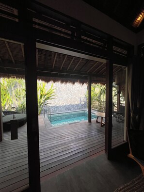 A covered outdoor area with a pool, wooden deck, and seating. - La Reserva Villas Bali (Jimbaran)