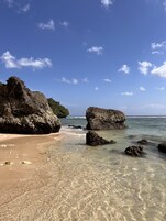 A beach with clear shallow waters, large rocks, and a sandy shore.