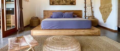 A bedroom with a large bed, a wooden headboard, a woven rug, and a wall-mounted artwork.