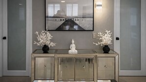 Ein modernes Interieur mit einem gerahmten Kunstwerk über einem Konsolentisch mit Spiegel, flankiert von zwei Vasen mit weißen Blumen.