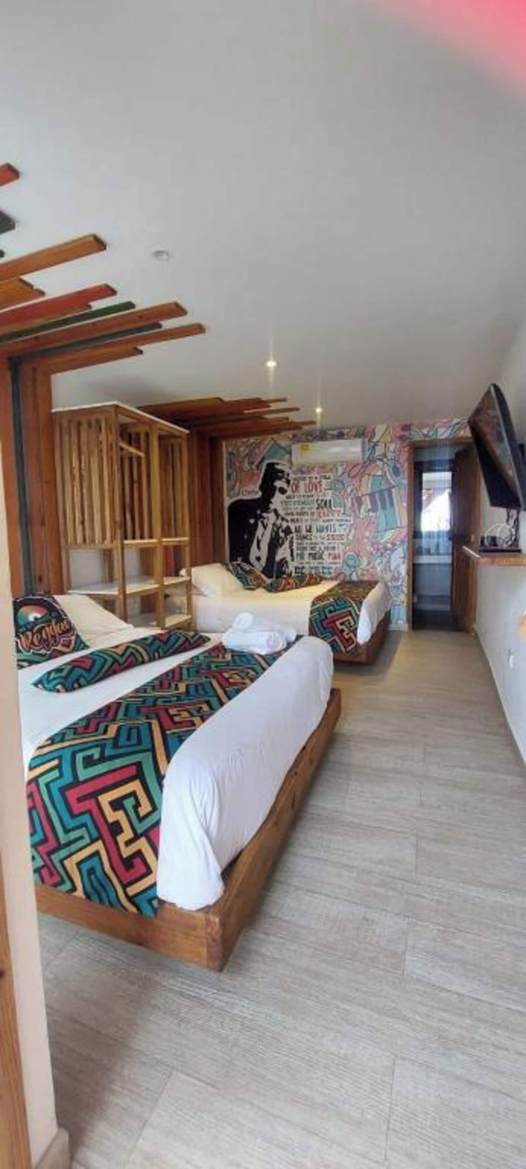 Un dormitorio con dos camas, cabeceros de madera, un mural en la pared y un televisor sobre un mueble.