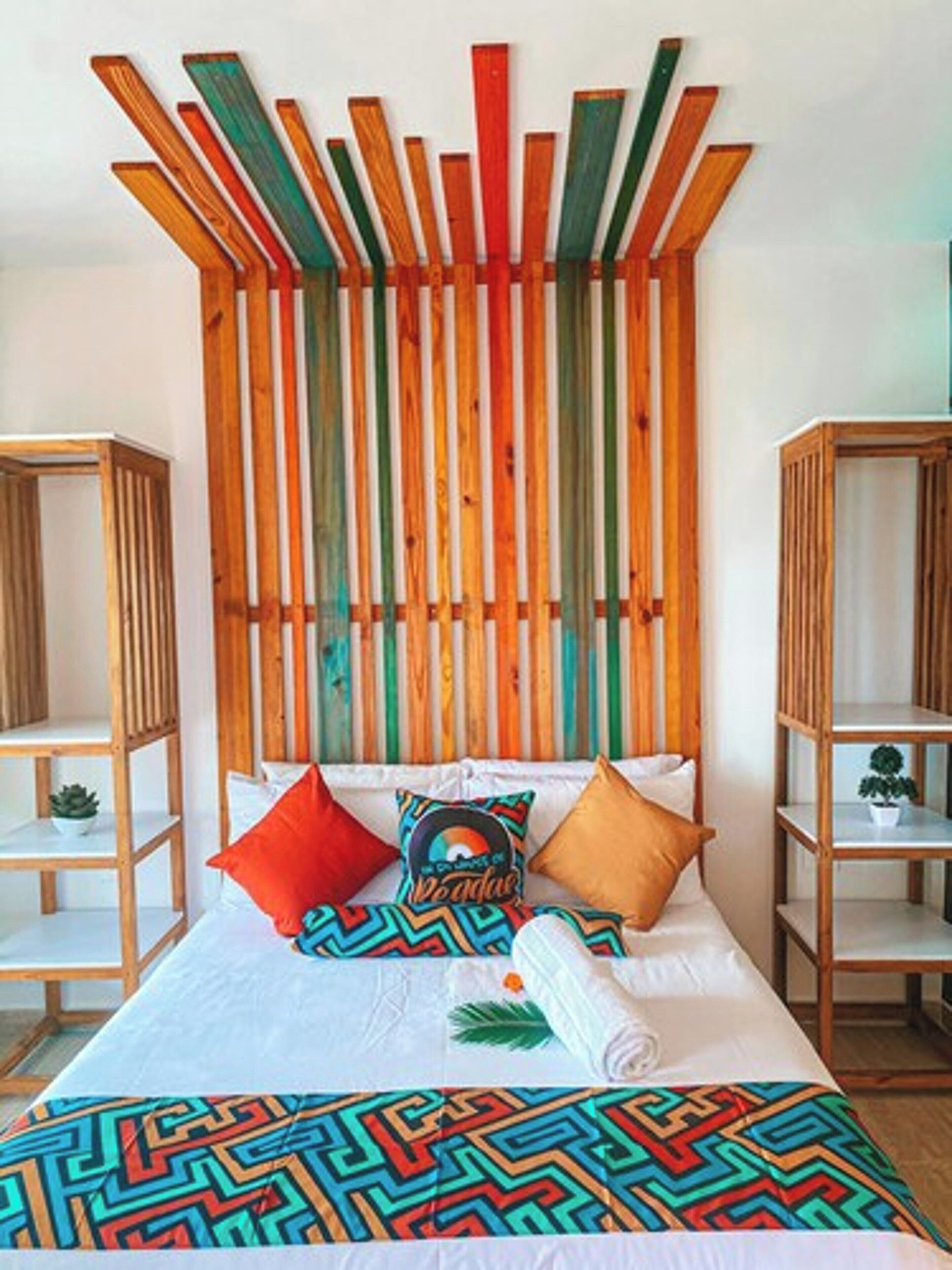 A bed with a colorful geometric-patterned bedspread, two pillows, and a decorative pillow with a vinyl record design.