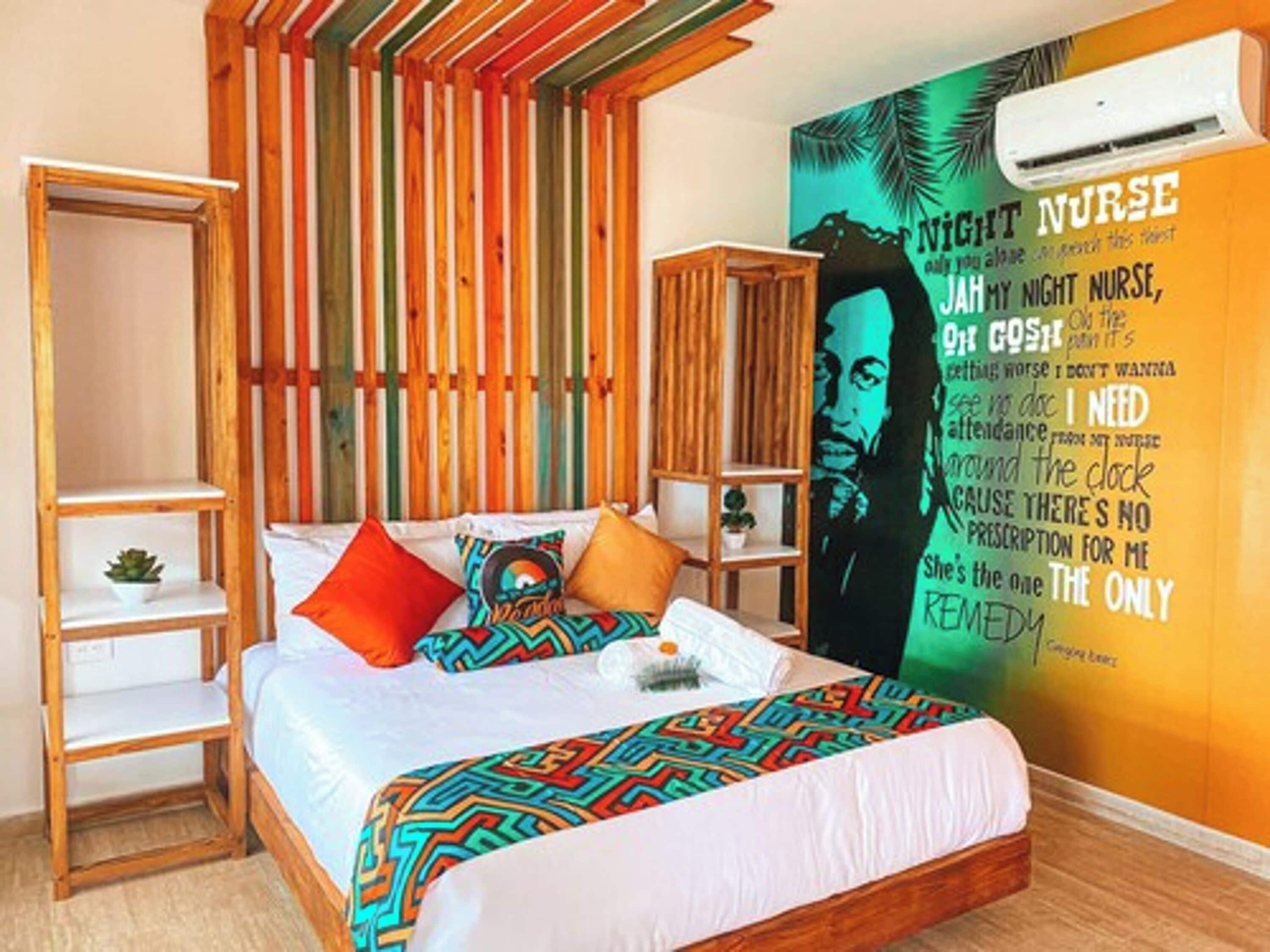Een slaapkamer met een bed, een houten plank, een wandairconditioner en een kleurrijke muurschildering.