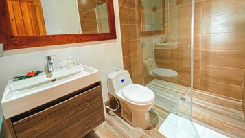 Un baño con un lavamanos blanco, tocador de madera, inodoro y cabina de ducha de vidrio.