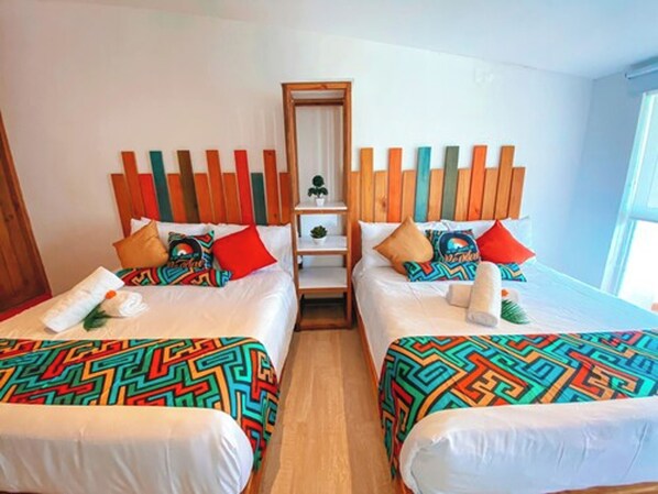 A hotel room with two beds, colorful patterned bedspreads, a wooden headboard, and a small shelf with a plant.