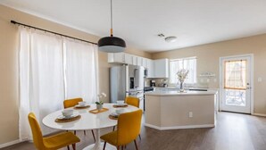 Una cuina moderna amb armaris blancs, una illa central i una zona de menjador amb una taula rodona i cadires grogues.
