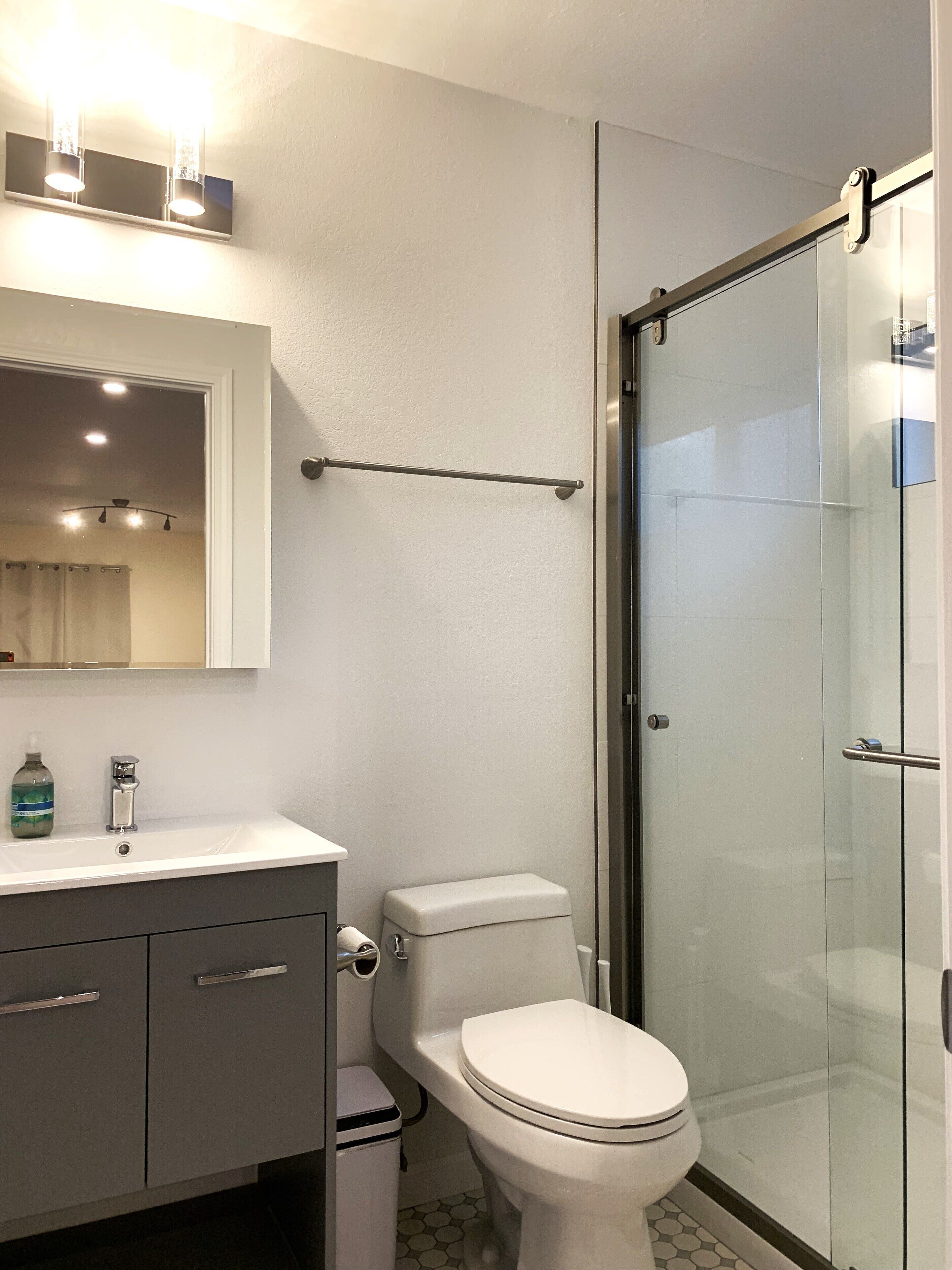 A modern bathroom with a glass shower enclosure, a white toilet, and a vanity with a mirror and lighting.