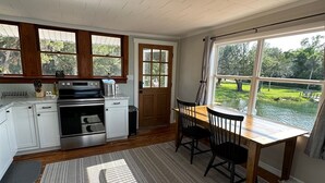 A kitchen with a dining table and chairs, a large window with a view of greenery, and a ceiling with recessed lighting.