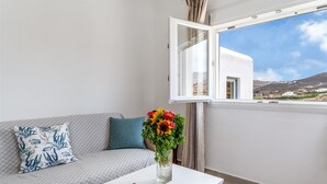 Un balcon avec un canapé blanc, un vase de fleurs et une vue dégagée sur un immeuble et un paysage.