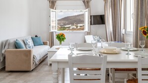 Une pièce comprenant une table à manger dressée pour deux personnes, un canapé, une fenêtre avec vue et un téléviseur à écran plat fixé au mur.