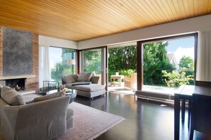 Una sala de estar moderna con chimenea, un sofá, una mesa de comedor y grandes puertas correderas de vidrio hacia un jardín.
