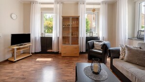 Een woonkamer met een flatscreen televisie, een kast met glazen, een bank en een salontafel.