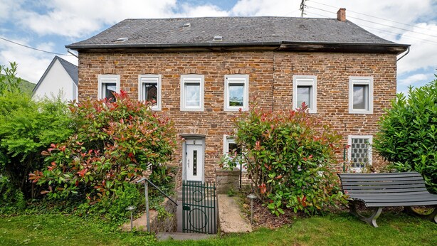 Een stenen huis met een voordeur, ramen en een bankje in de voortuin.