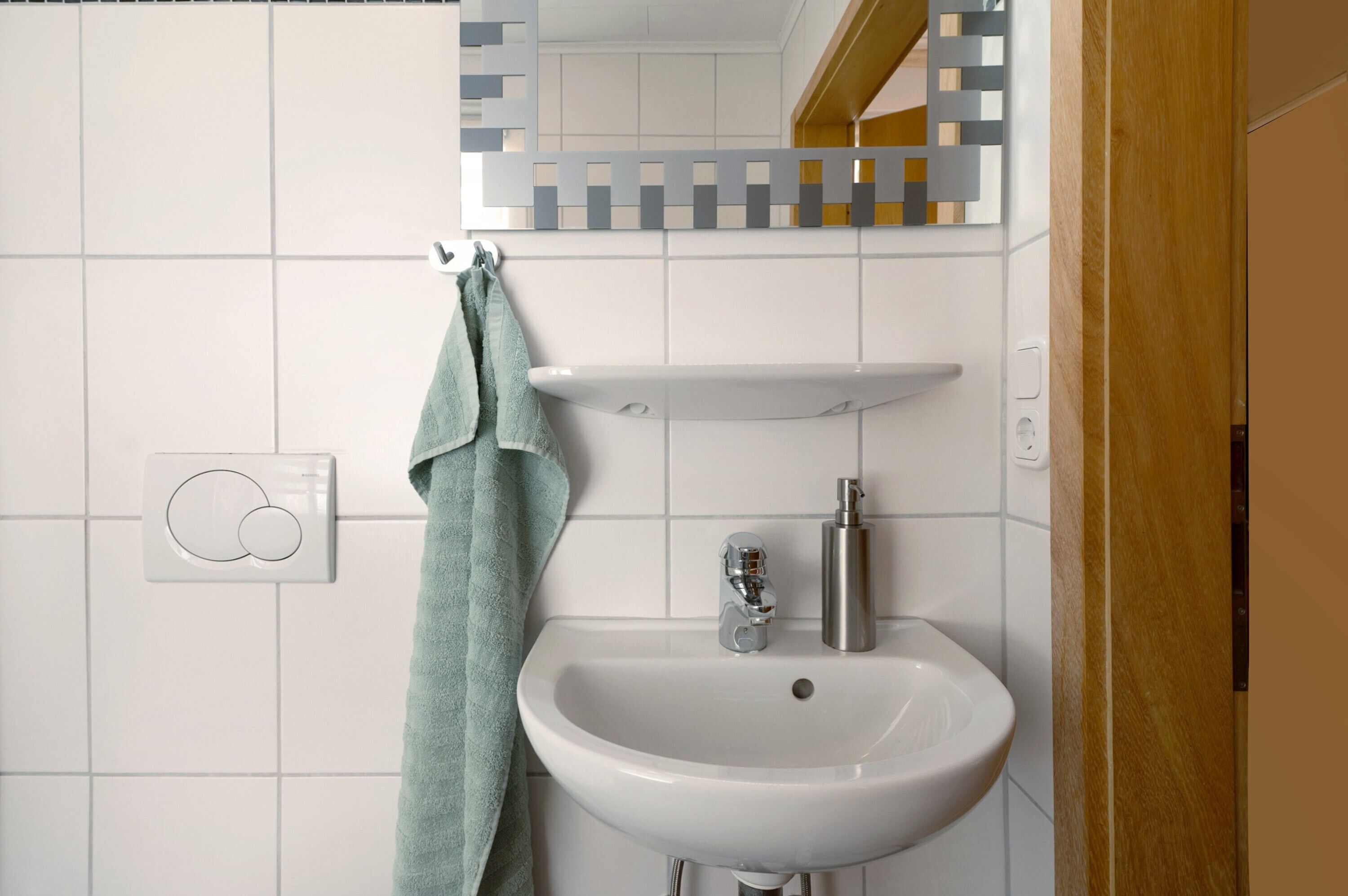 Une salle de bain avec un lavabo blanc, un miroir doté d’un cadre géométrique et une serviette suspendue à un porte-serviettes.