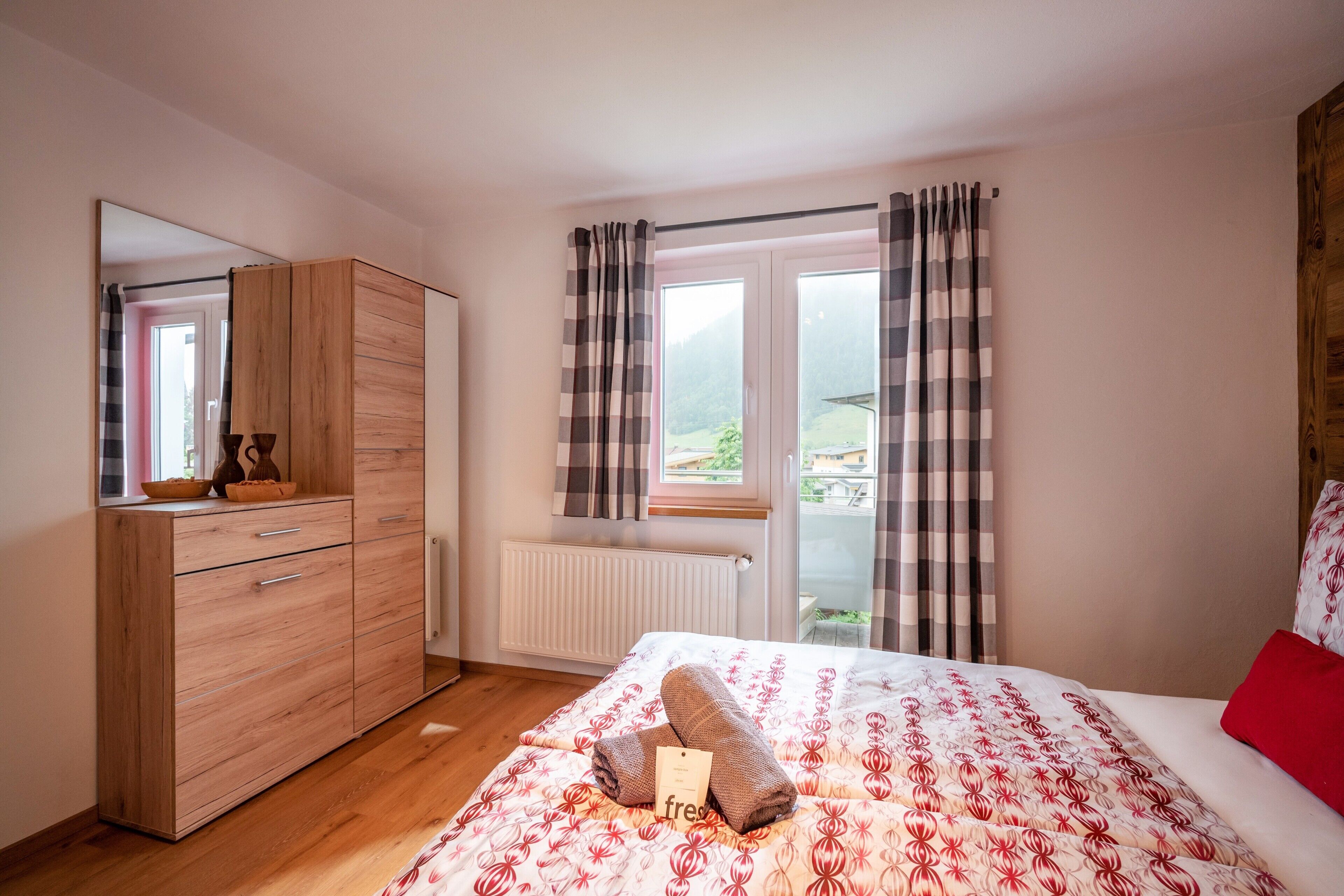 Ein Schlafzimmer mit einem Bett, einem Holzschrank, einem Heizkörper und einem Fenster mit Vorhängen.