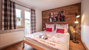 A bedroom with a wooden headboard, a bed with red and white bedding, a bedside lamp, and a window with curtains. - Apartment 'Eve' with Mountain View, Balcony and Wi-Fi (Söll)