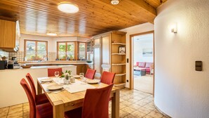 A dining area with a wooden table and red chairs, a kitchen with wooden cabinets, and a view of the outdoors.