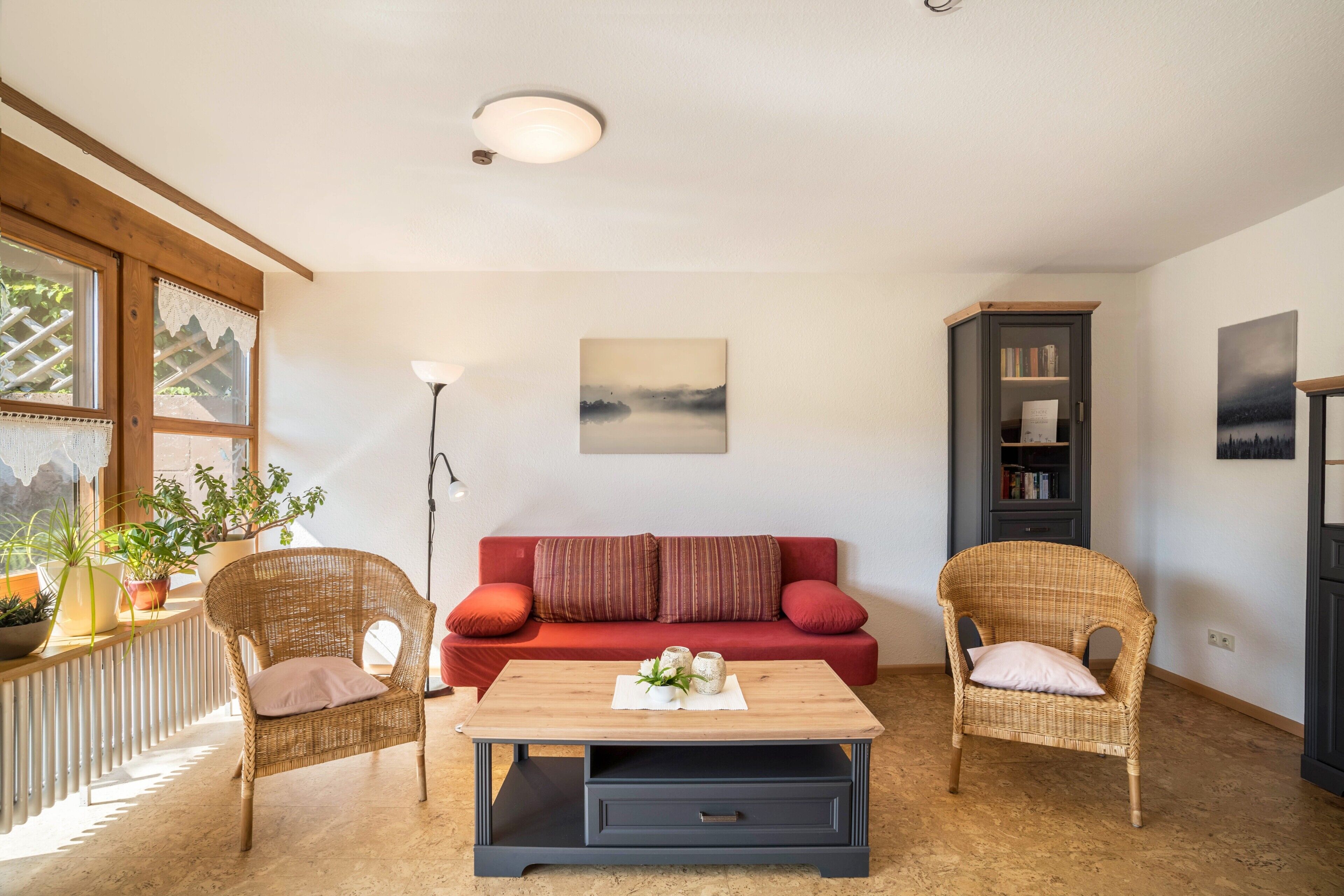 A cozy living room with a red sofa, wicker chairs, a wooden coffee table, and a bookshelf.