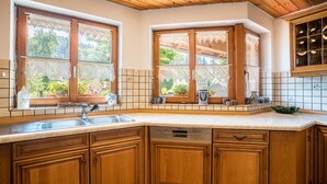 A kitchen with wooden cabinets, a dishwasher, and two windows with lace curtains.