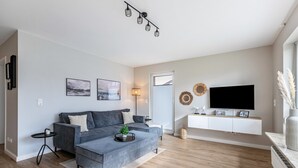 A modern living room with a sofa, coffee table, TV, and decorative wall art. - Apartment "Haus Dünenbutze" with Shared Garden & Wi-Fi (Büsum)