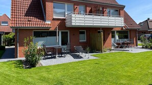 A two-story house with a balcony, a patio with outdoor furniture, and a well-maintained lawn. - Apartment "Haus Dünenbutze" with Shared Garden & Wi-Fi (Büsum)
