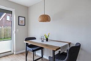 Uma sala de jantar com uma mesa de madeira, duas cadeiras, um lustre pendente e um pequeno vaso com planta.