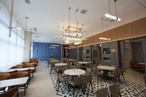 A modern hotel lobby with round tables and chairs, a patterned floor, and a blue wall in the background. - J.SKY HOTEL (Wuhan)