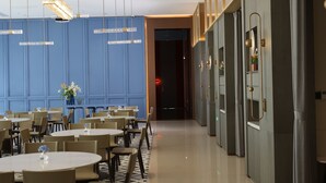 Um hall de hotel moderno com mesas e cadeiras redondas, uma parede azul com sinalização e um espelho com moldura decorativa.