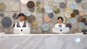 Duas pessoas no balcão de recepção, com uma parede decorada por pratos redondos atrás delas.