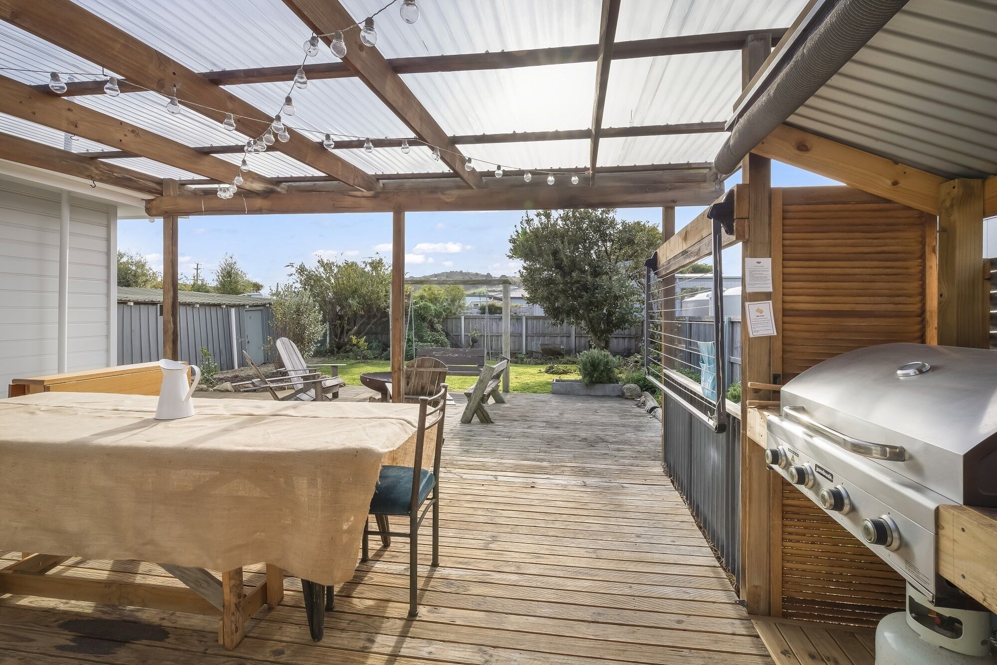 A covered outdoor patio with a wooden table, chairs, and a barbecue grill.
