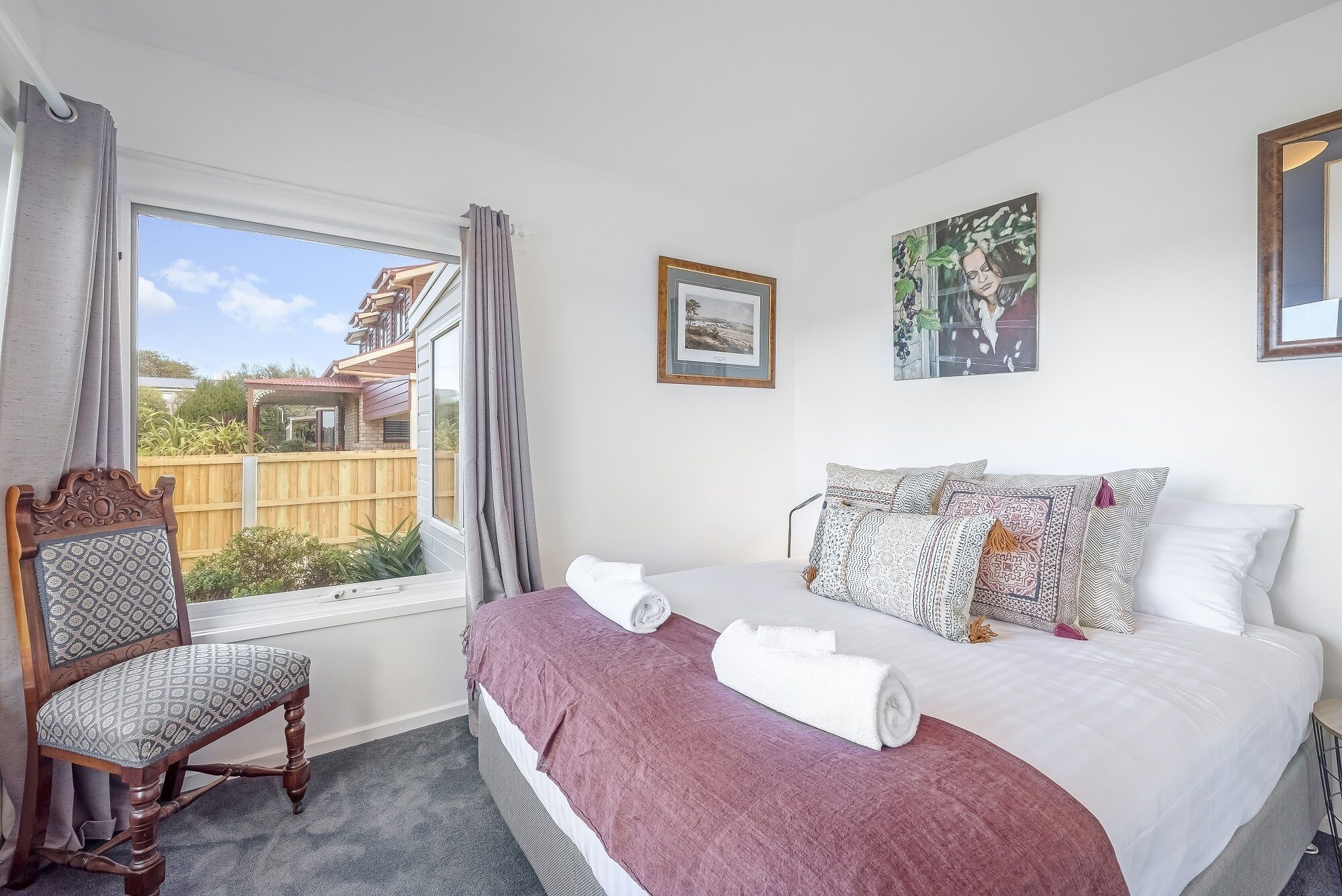 A bedroom with a large bed, a chair, a window, and two framed pictures on the wall.